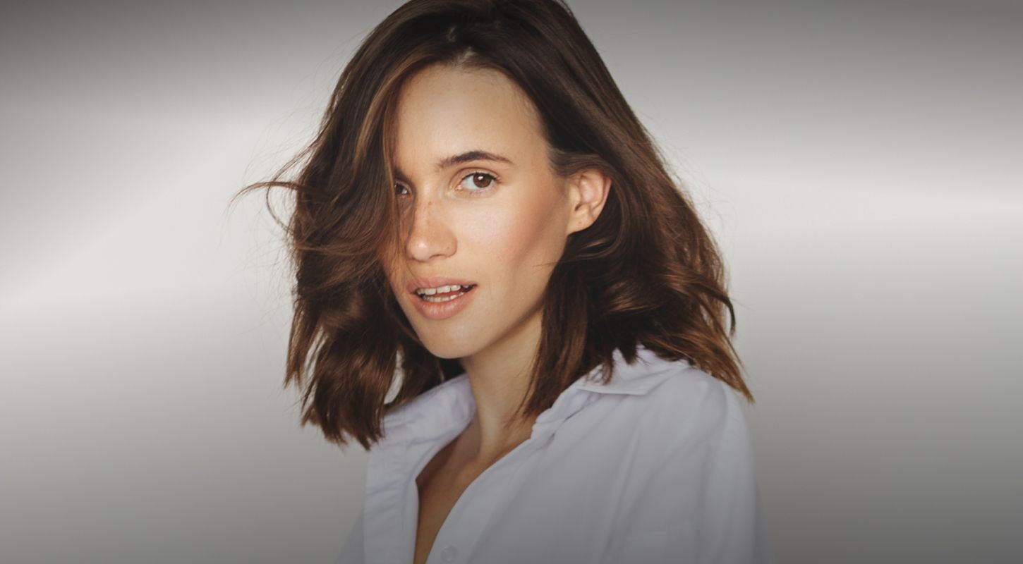 Woman smiling with tousled hair in white shirt.