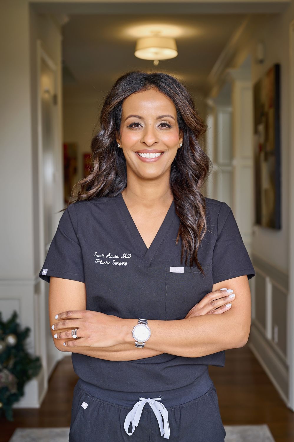 Smiling doctor in scrubs indoors, arms crossed.