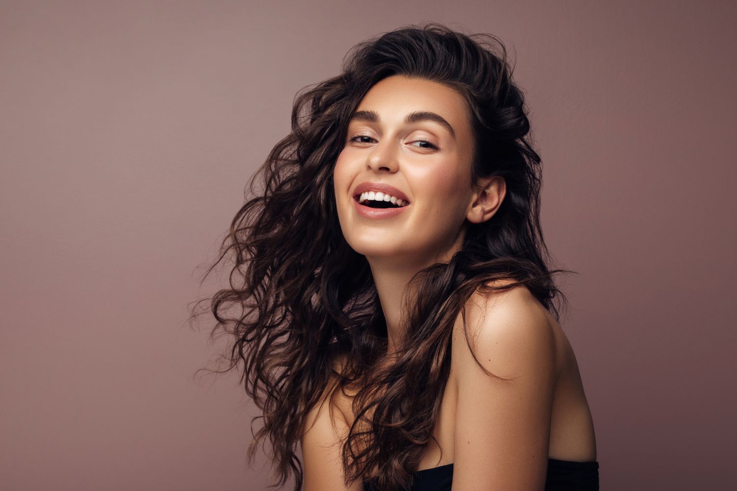 Smiling woman with wavy hair on neutral background